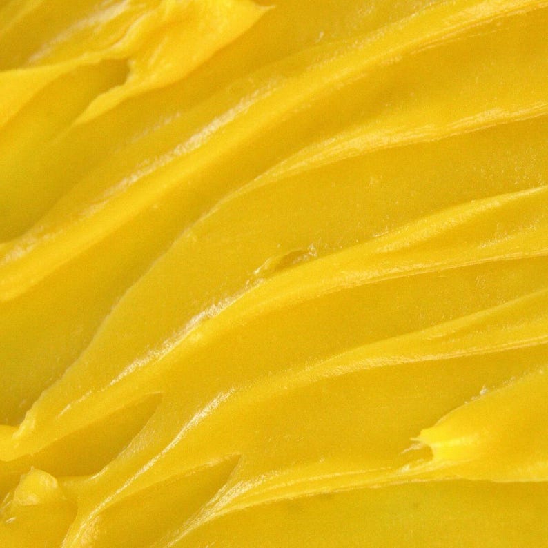 May include: A thick, vibrant yellow substance with a smooth, creamy texture. The surface features distinct, sweeping ridges and peaks created by a tool or utensil, showing a consistent, semi-solid consistency throughout the entire frame.