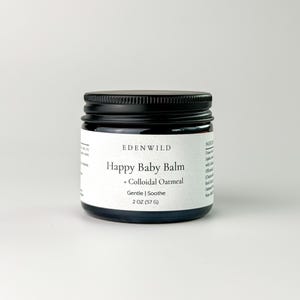 Puede incluir: Un pequeño frasco de vidrio oscuro con tapa negra. La etiqueta dice "EDENWILD Happy Baby Balm + Colloidal Oatmeal Gentle | Soothe". El frasco contiene 57 g de producto. Fondo claro y liso.