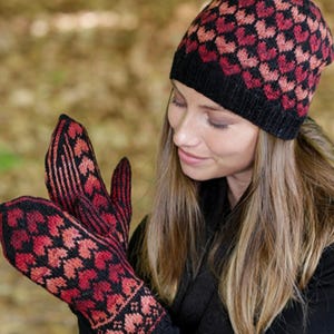 Peut inclure: Un bonnet tricoté et une paire de moufles assorties présentant un motif de cœurs répétitifs dans des tons de rouge, orange et noir. Le bonnet possède un bord côtelé noir uni, tandis que les moufles affichent un motif géométrique détaillé.