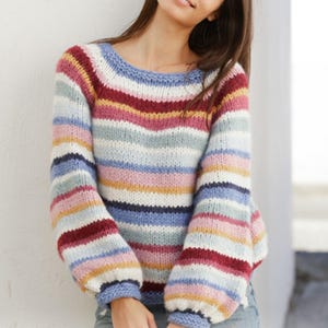 Pode incluir: Um suéter listrado com decote redondo e mangas compridas. O suéter apresenta listras horizontais em várias cores, incluindo azul, branco, vermelho, rosa e amarelo. As mangas têm formato de balão. O suéter é feito de malha.