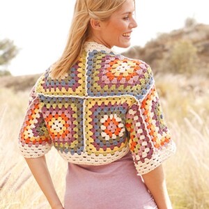 Könnte beinhalten: Ein farbenfrohes, gehäkeltes Bolero-Jäckchen. Die Jacke hat ein Patchwork-Design mit Quadraten in Orange-, Lila-, Gelb- und Blautönen mit cremefarbenem Besatz. Das kurzärmelige Kleidungsstück wird von einer Person auf einem Feld getragen.