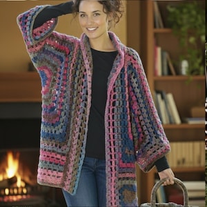 May include: A colourful, open-weave crochet cardigan in shades of pink, blue, brown, and grey. The long-sleeved garment has a collar and a loose fit. The cardigan is worn over a black top and blue jeans.