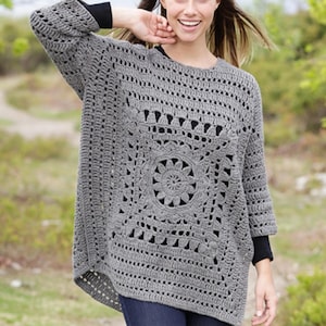 May include: A gray, open-weave crochet sweater with a square floral design on the front. The sweater has three-quarter sleeves and a loose, comfortable fit. The model is wearing a black undershirt.