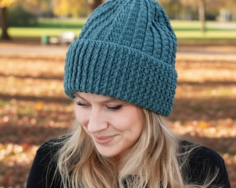 Peut inclure: Un bonnet en tricot de couleur teal avec un bord côtelé. Le bonnet est fait d'un fil texturé et possède un bord replié. Ce bonnet est conçu pour garder la tête au chaud.