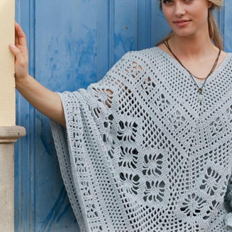 Op de afbeelding: Een lichtblauwe gehaakte poncho met een V-hals. De poncho heeft een open patroon met bloemmotieven. Het kledingstuk is gemaakt van een zacht, lichtgewicht materiaal, perfect om te dragen.