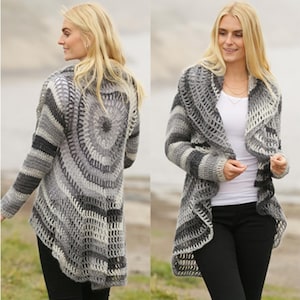 Op de afbeelding: Een grijze, witte en zwarte gehaakte cardigan met een uniek cirkelvormig ontwerp op de rug. De open vest heeft een sjaalkraag en lange mouwen. Het kleurenpalet omvat verschillende tinten grijs en wit, waardoor een gestructureerd, gestreept patroon ontstaat.