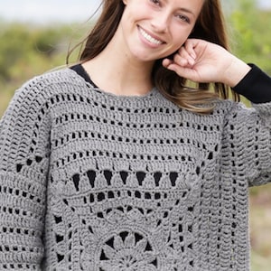 May include: A gray crochet sweater with a round neckline and long sleeves. The sweater features an openwork design with a floral pattern on the lower front. The sleeves and upper chest have a repeating pattern of small openings.