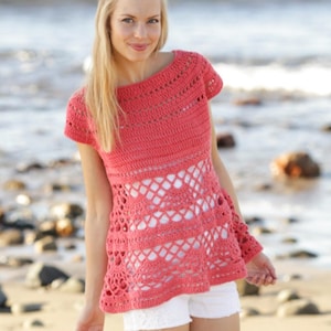 May include: Coral-colored crochet top with a unique openwork design. The short-sleeved top features a round neckline and a flared hem. The intricate crochet pattern creates a visually appealing texture. The top is paired with white shorts, perfect for a beach or summer look.