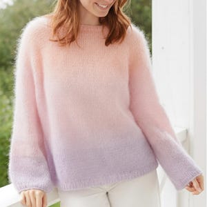 Puede incluir: Un suéter suave y de gran tamaño en un degradado de rosa y lavanda. El jersey de manga larga tiene cuello redondo y una textura difusa. El suéter se usa con pantalones blancos y es adecuado para ropa casual.