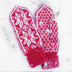 Puede incluir: Un par de mitones de punto rojos y blancos con un diseño de copo de nieve. Los mitones están en la nieve, con los puños doblados. Un accesorio de invierno.