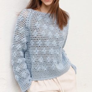 May include: A light blue crochet sweater with a round neckline and long sleeves. The sweater has a textured, open-weave design. The garment is made of a soft, lightweight material, perfect for layering.