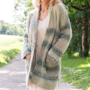 May include: A long, open-front cardigan in a soft, textured knit. The color palette includes shades of green, blue, and beige, creating a striped pattern. The cardigan features two front pockets and a relaxed fit, perfect for layering.