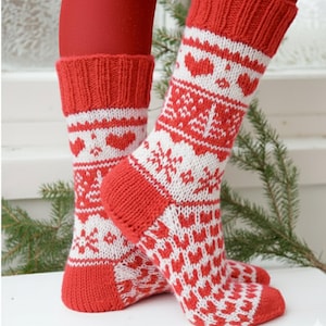 May include: Red and white knit socks with a heart and snowflake pattern. The socks have a ribbed cuff and a red heel and toe. The design features a repeating pattern of white hearts and snowflakes on a red background. The socks are displayed on a white surface.