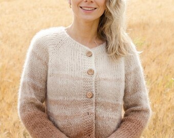 Könnte beinhalten: Knopf-Cardigan in einem Farbverlauf von Creme nach Braun. Der langärmlige Pullover hat einen runden Ausschnitt und ist aus einem weichen, strukturierten Garn gefertigt. Der Cardigan wird über einem weißen Kleidungsstück getragen, mit einem Weizenfeld im Hintergrund.