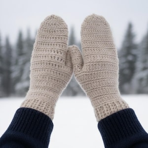 May include: A pair of beige crochet mittens with a ribbed cuff, set against a snowy backdrop. The mittens are made of a textured yarn, offering a warm and cozy appearance. The cuffs are a dark navy blue.