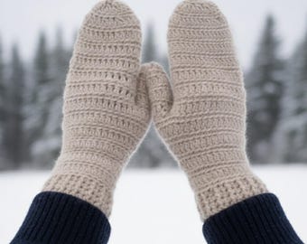 以下が含まれることがあります： 雪景色を背景に、ベージュ色の編み物ミトン。リブ編みの袖口が特徴で、暖かく居心地の良い印象を与えます。ミトンは質感のある糸で編まれ、袖口は濃いネイビーブルーです。