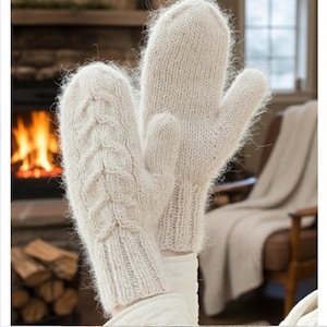 May include: A pair of off-white knitted mittens. One mitten features a cable knit design. The mittens are made of a soft, fuzzy yarn. The background includes a fireplace and a cozy setting.