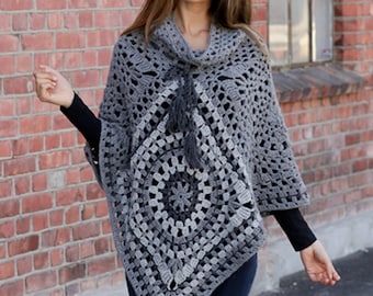 Puede incluir: Un poncho de ganchillo gris con cuello alto y diseño cuadrado. El poncho presenta un patrón circular central y un detalle de borla. Las mangas son abiertas y la prenda está hecha de un hilo suave y texturizado.