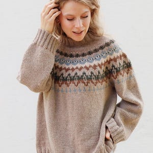 May include: A beige knit jumper featuring a high mock neck and long sleeves with ribbed cuffs. The upper chest and shoulder area display a horizontal band with a geometric pattern in shades of dark brown, light blue, and muted green.