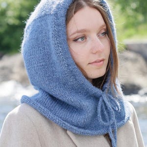 Pode incluir: Uma balaclava de malha em azul poeirento feita com fio texturizado, apresentando uma borda canelada ao longo da abertura do rosto e um cordão de ajuste a condizer no pescoço. A peça oferece cobertura total para a cabeça e o pescoço.