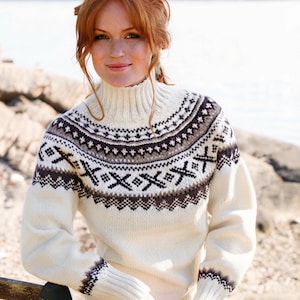 May include: A cream-coloured long-sleeve jumper featuring a high ribbed turtleneck collar and ribbed cuffs. The garment displays a dark brown and grey geometric pattern encircling the chest, shoulders, and upper back, with matching bands at the wrists.