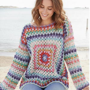 May include: A multi-coloured crochet sweater featuring a square pattern in shades of red, orange, yellow, green, blue, and purple. The long-sleeved sweater has a round neckline and a relaxed fit.