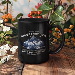 May include: Black ceramic mug featuring the text "Donner Party Tours" and a mountain graphic. The mug also includes the text "Survival Not Guaranteed, Take a Shortcut with Us, 55% Success Rate." The mug is surrounded by floral arrangements.