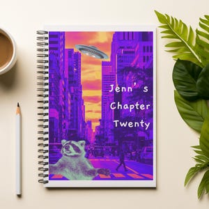 May include: A spiral-bound notebook with a cover depicting a raccoon, a flying saucer, and a cityscape in purple and orange. The text "Jenn's Chapter Twenty" is on the cover. A cup of coffee and a pencil are next to the notebook.