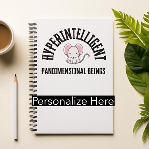 May include: A white spiral-bound notebook with the text "HYPERINTELLIGENT PANDIMENSIONAL BEINGS" and a cartoon mouse illustration. The notebook has a black bar that says "Personalize Here". A cup of coffee and a pencil are next to the notebook.