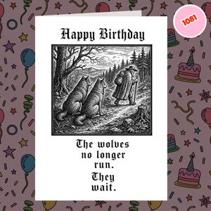 May include: A white greeting card featuring a black and white illustration of two wolves sitting on a path watching a traveller with a walking stick. The text reads Happy Birthday at the top and The wolves no longer run. They wait. at the bottom.