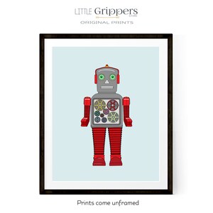 May include: A framed print featuring a retro robot illustration. The robot is primarily red and gray, with green eyes and a detailed gear design on its chest. The background is a light blue, and the print is framed in black. Text at the top reads "LITTLE Grippers STORE ORIGINAL PRINTS".
