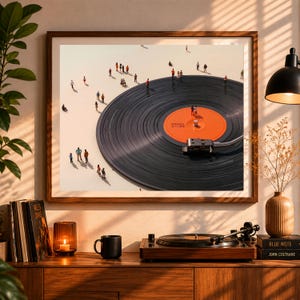 May include: A framed art print depicts a large vinyl record with miniature figures on its surface. The record has an orange label and is set against a light background. A record player and other decor are on a wooden cabinet below the print.