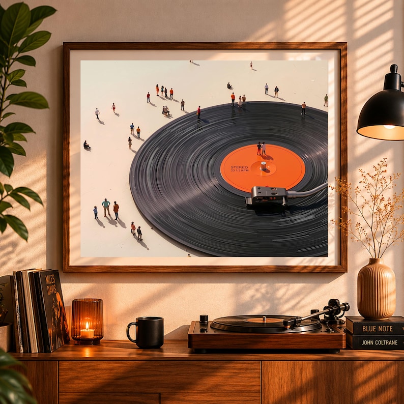 May include: A framed art print depicts a large vinyl record with miniature figures on its surface. The record has an orange label and is set against a light background. A record player and other decor are on a wooden cabinet below the print.
