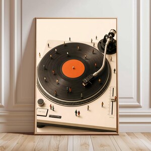 May include: A framed wall art print featuring a high-angle view of a cream-colored turntable with a black vinyl record. The record has a bright orange center label. Tiny miniature figures of people are standing across the surface of the record.