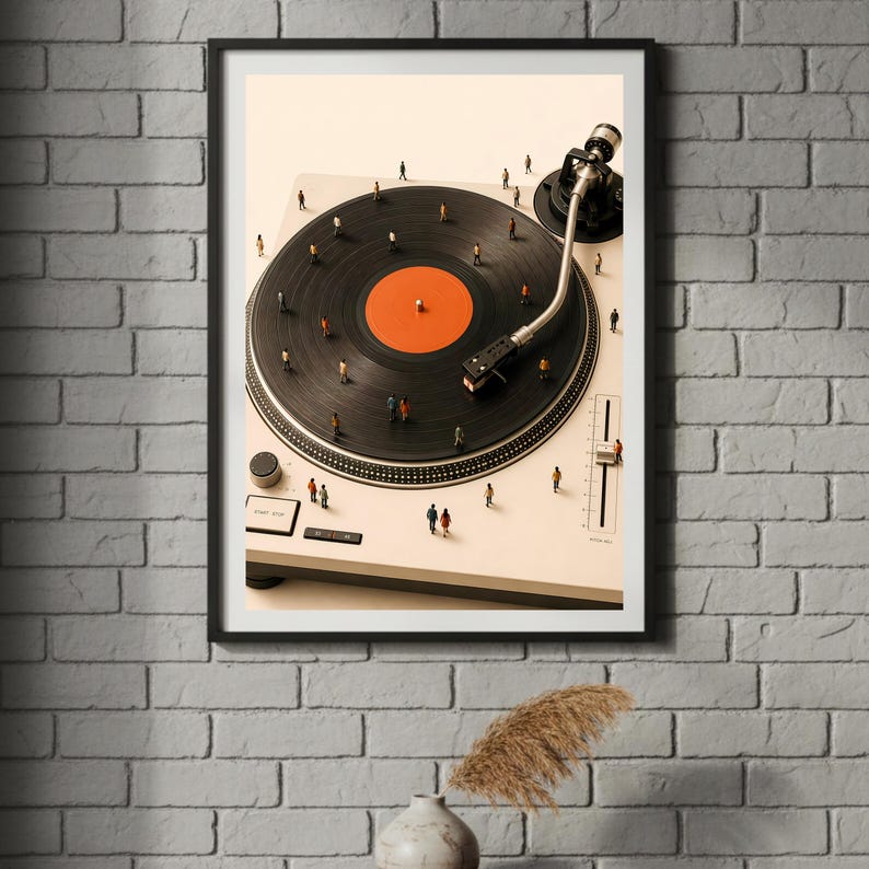May include: A framed wall art print featuring a high-angle view of a white turntable with a black vinyl record. The record has a bright orange center label. Tiny miniature figures of people are scattered across the record and the turntable surface.
