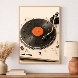 May include: A framed wall art print depicting a cream-colored turntable with a black vinyl record featuring an orange center label. Tiny miniature figures of people are scattered across the surface of the record and the turntable base.
