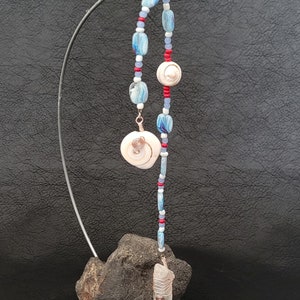 May include: A white and blue beaded necklace with red accents and two white shell charms hanging from a metal stand.