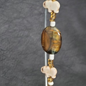 May include: A gold and white beaded necklace with a tiger's eye bead and white elephant charms.