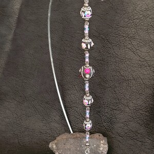 May include: A silver wire bookmark with a purple crystal charm and black beads with pink and white floral designs.