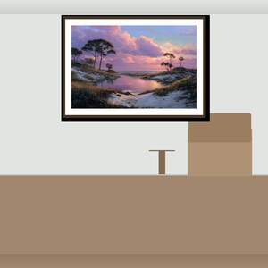 May include: A framed landscape painting showing a coastal scene with a body of water reflecting a sunset. The artwork features trees, sand, and a sky filled with pink and purple clouds. The frame is dark brown.