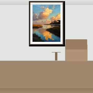 May include: A framed landscape painting shows a tranquil waterscape with a colourful sky and clouds. The artwork features a river reflecting the sky's colours, with trees and marshy banks. The frame is black.