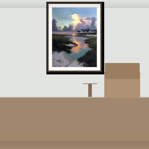 May include: A framed landscape painting shows a tranquil coastal scene with a river reflecting a vibrant sunset. The artwork is displayed on a light grey wall above a brown table. A small, brown, T-shaped object and a brown box are on the table.