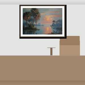 May include: A framed landscape painting shows a sunset over a calm lake, with palm trees and other plants. The artwork is in a dark brown frame, mounted on a light grey wall. A small table and a box are below the painting.