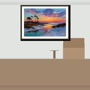 May include: Framed landscape art depicting a sunset over a beach with silhouetted trees. The sky transitions from blue to orange and pink, reflected in the water. The artwork is displayed on a light grey wall.