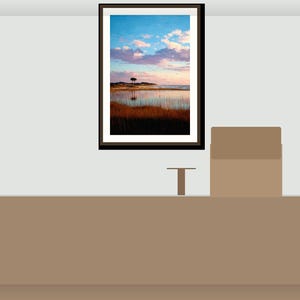 May include: A framed landscape painting showing a coastal scene. The artwork features a vibrant sky with blue and pink hues, a calm body of water, and a lone tree on the horizon. The frame is dark brown.