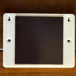 May include: A white rectangular magnet with a dark brown magnetic surface. The white frame has four holes for hanging. This item is designed for displaying photos, notes, or other lightweight items on a metal surface.