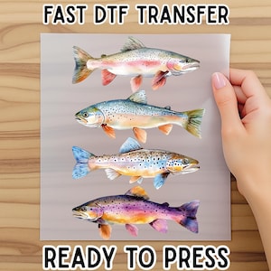 May include: A sheet featuring four colorful fish illustrations, ready for heat transfer. The fish are in shades of pink, blue, purple, and orange. The text "FAST DTF TRANSFER" and "READY TO PRESS" are printed on the sheet.