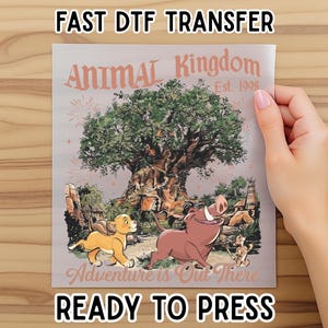 May include: A DTF transfer featuring the Animal Kingdom logo with the Tree of Life, Simba, Pumbaa, and Timon. The text reads "Adventure is Out There" and "Ready to Press". The transfer is held by a hand.