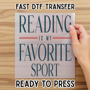 May include: A white DTF transfer with the text "READING IS MY FAVORITE SPORT" in navy blue, with red lines. The transfer also includes the text "FAST DTF TRANSFER" and "READY TO PRESS" in black.