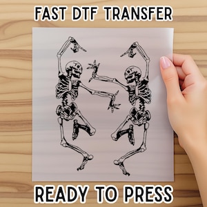 May include: A DTF transfer sheet featuring a black and white illustration of two skeletons dancing. The text "FAST DTF TRANSFER" and "READY TO PRESS" are printed at the top and bottom of the sheet.